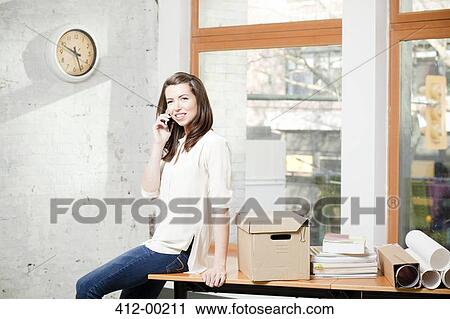 Stock Image - Businesswoman talking on cell phone in office. Fotosearch