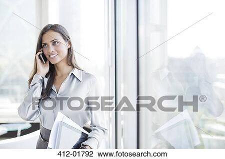 Stock Image - Businesswoman talking on cell phone in office. Fotosearch
