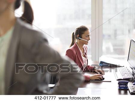 Stock Photo - Businesswoman wearing headset at desk. Fotosearch