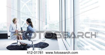 Stock Image - Businesswomen talking in office lobby. Fotosearch