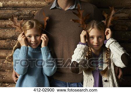 Stock Image - Girls using leaves as antlers with father. Fotosearch