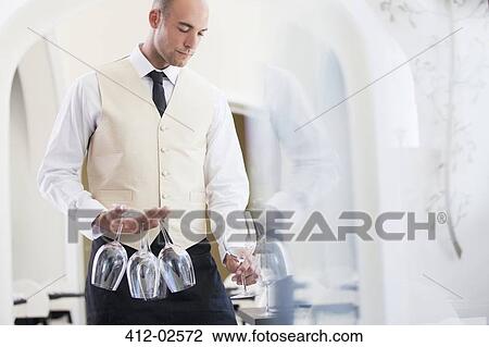 Stock Image - Waiter carrying wine glasses in restaurant. Fotosearch