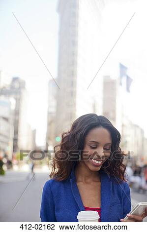 Stock Image - Woman using cell phone on city street. Fotosearch