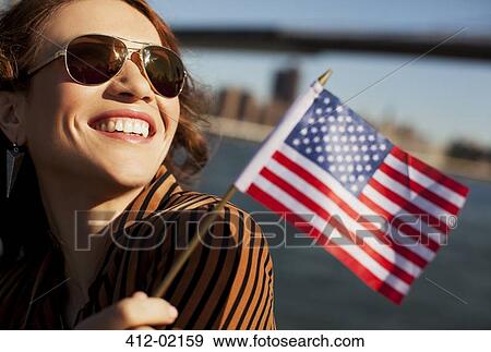 Stock Photo - Woman waving American flag by urban bridge. Fotosearch