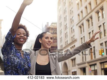 Stock Image - Women hailing taxi on city street. Fotosearch