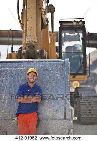 Worker standing by digger on site View Large Photo Image Stock Image - Worker standing by digger on site. Fotosearch