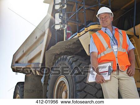 Worker standing by machinery on site View Large Photo Image Stock Photograph - Worker standing by machinery on site. Fotosearch