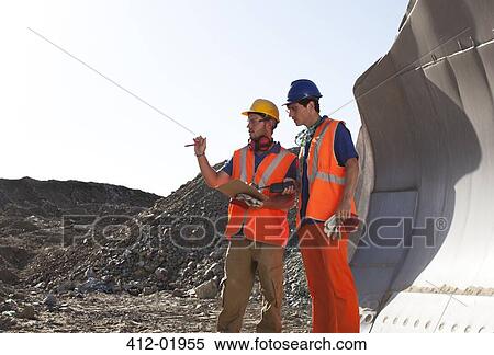 Workers talking by machinery in quarry View Large Photo Image Stock Photography - Workers talking by machinery in quarry. Fotosearch