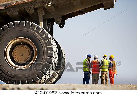 Stock Image - Workers talking by machinery on site. Fotosearch