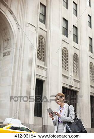 Picture - Businesswoman using tablet computer on city street. Fotosearch