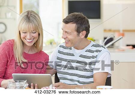 Couple using tablet computer at table View Large Photo Image Stock Photograph - Couple using tablet computer at table. Fotosearch