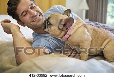 Stock Image - Dog licking man's face on bed. Fotosearch