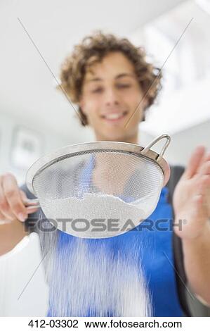 Stock Image - Man sifting flour in kitchen. Fotosearch