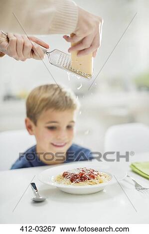 Stock Photo - Mother grating cheese over son's spaghetti. Fotosearch