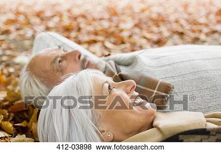 Stock Photo - Older couple laying in autumn leaves. Fotosearch
