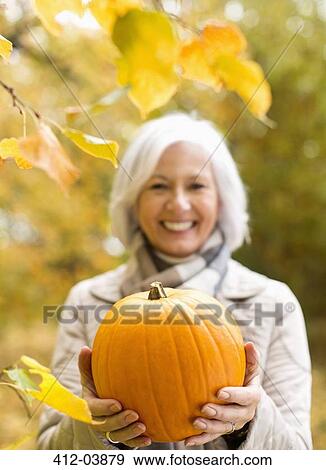 Older woman holding pumpkin in park View Large Photo Image Stock Photo - Older woman holding pumpkin in park. Fotosearch