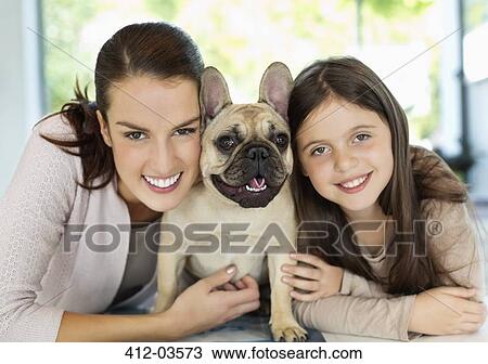 Stock Image - Smiling mother and daughter hugging dog. Fotosearch