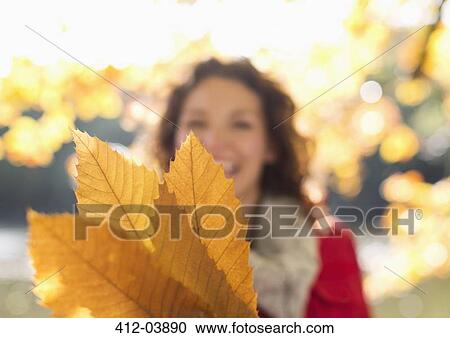Stock Image - Woman holding autumn leaves in park. Fotosearch