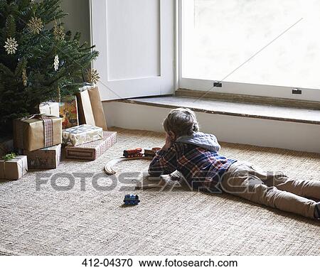 Stock Image - Boy playing with trains by Christmas tree. Fotosearch