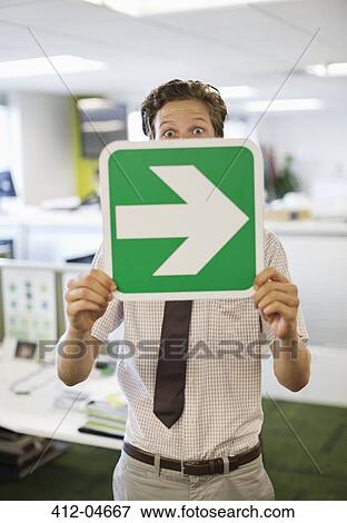 Stock Photo - Businessman holding arrow sign in office. Fotosearch