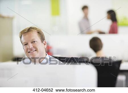 Stock Image - Businessman smiling at desk. Fotosearch