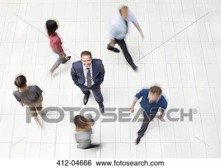 Businessman standing in busy office hallway View Large Photo Image Stock Photograph - Businessman standing in busy office hallway. Fotosearch