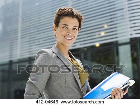 Stock Photograph - Businesswoman carrying folders outdoors. Fotosearch