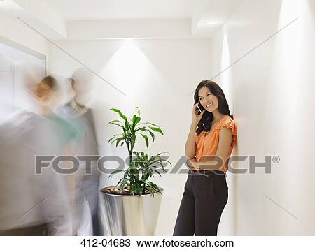 Businesswoman talking on cell phone in busy office hallway View Large Photo Image Stock Image - Businesswoman talking on cell phone in busy office hallway. Fotosearch