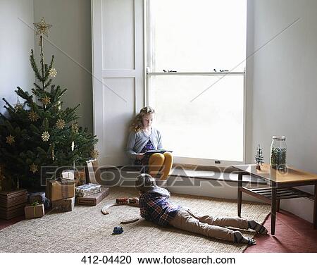 Stock Image - Children relaxing by Christmas tree. Fotosearch