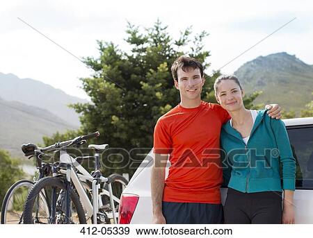 Stock Photo - Couple smiling by car in rural landscape. Fotosearch