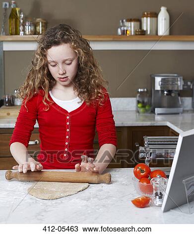 Stock Image - Girl rolling dough in kitchen. Fotosearch