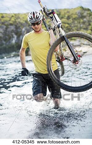 Stock Photography - Man carrying mountain bike in river. Fotosearch