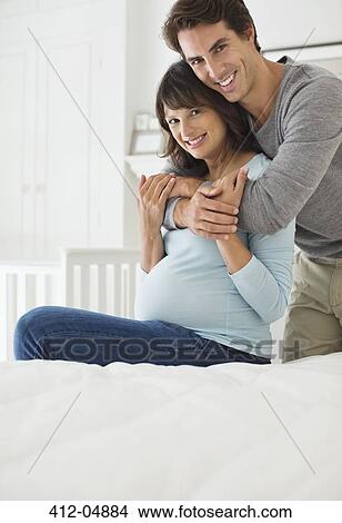 Picture - Man hugging pregnant girlfriend on bed. Fotosearch