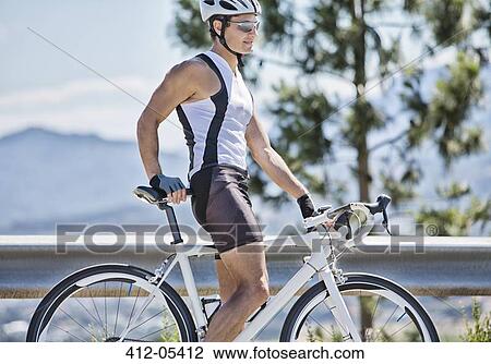 Stock Image - Man standing on bicycle on rural road. Fotosearch