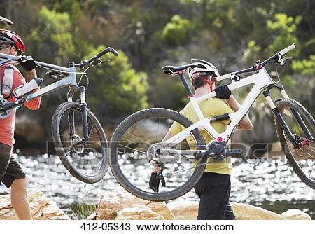 Stock Image - Men carrying mountain bikes in river. Fotosearch