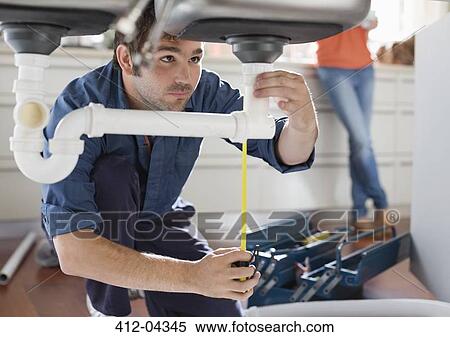 Stock Photography - Plumber working on pipes under kitchen sink. Fotosearch