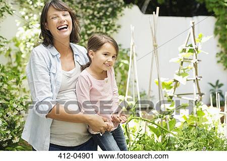 Stock Image - Pregnant mother and daughter gardening together. Fotosearch
