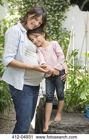 Stock Image - Pregnant mother and daughter hugging outdoors. Fotosearch