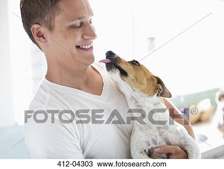 Stock Image - Smiling man holding dog. Fotosearch