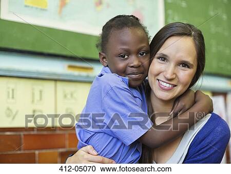 Stock Image - Teacher hugging student in class. Fotosearch