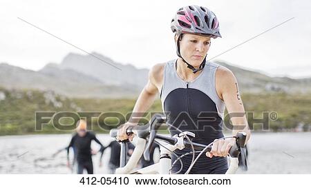 Stock Image - Woman pushing bicycle on beach. Fotosearch