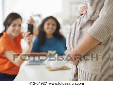 Woman taking picture of pregnant friend's bell View Large Photo Image Stock Photo - Woman taking picture of pregnant friend's bell. Fotosearch