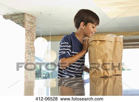 Stock Photo - Boy looking through paper bag in kitchen. Fotosearch