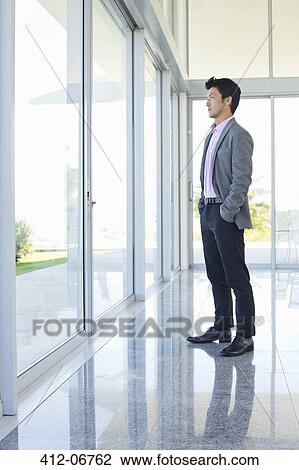 Businessman standing at office window View Large Photo Image Stock Image - Businessman standing at office window. Fotosearch
