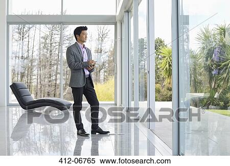 Businessman standing at office window View Large Photo Image Stock Photography - Businessman standing at office window. Fotosearch