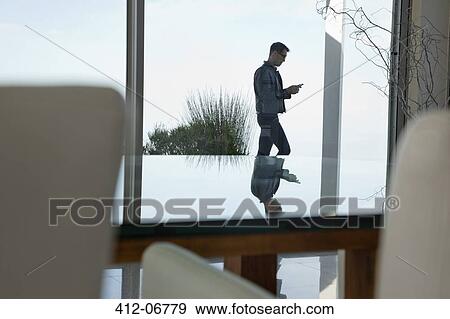Stock Photo - Businessman using cell phone at office window. Fotosearch