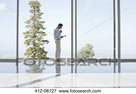 Businessman using tablet computer at office window View Large Photo Image Stock Photo - Businessman using tablet computer at office window. Fotosearch