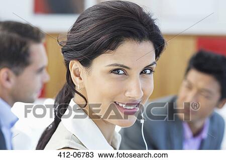 Stock Image - Businesswoman listening to headphones in office. Fotosearch