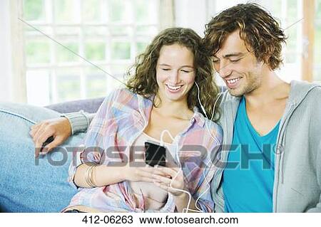 Couple listening to earphones together on sofa View Large Photo Image Stock Image - Couple listening to earphones together on sofa. Fotosearch