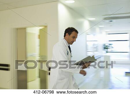 Doctor reading medical chart in hospital hallway View Large Photo Image Stock Photo - Doctor reading medical chart in hospital hallway. Fotosearch